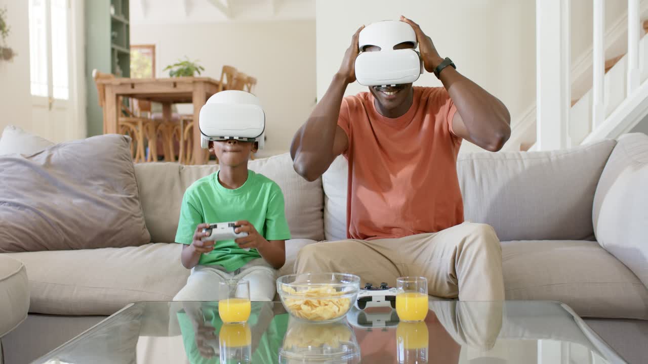 Padre e figlio afroamericani giocano alla VR a casa, il padre indossa il visore e si unisce con un gamepad.