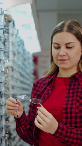 portrait of a beautiful woman in the eyewear store. young female in red shirt trying on new glasses. buyer in the optical shop. vertical video