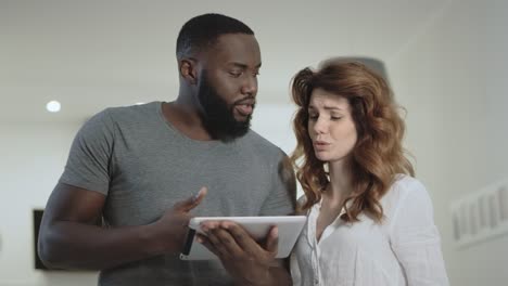 Young couple discussing at home kitchen together. Black man showing pictures