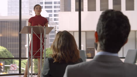 audience applaud young woman speaking at a business seminar