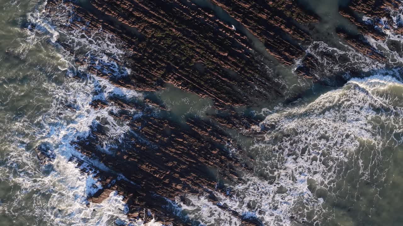 Waves Crashing Against A Rocky Shoreline In Ireland. - aerial overhead shot