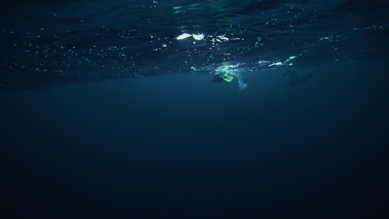 Diver silhouette swimming beneath Arctic ocean surface with bubbles rising above, slow motion