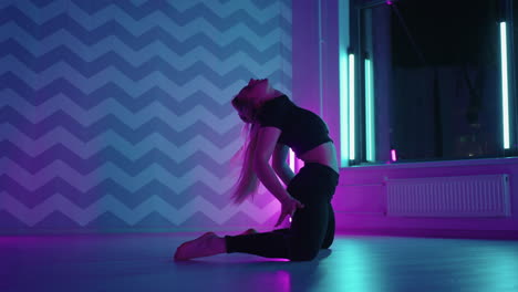 A-woman-dances-in-a-studio-with-a-neon-light-performing-graceful-exercises-and-movements-from-stretching-and-dancing-in-slow-motion