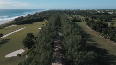 Vista-De-Drones-De-La-Carretera-Entre-Los-Pinos-Y-Cerca-Del-Campo-De-Golf-Junto-A-La-Playa