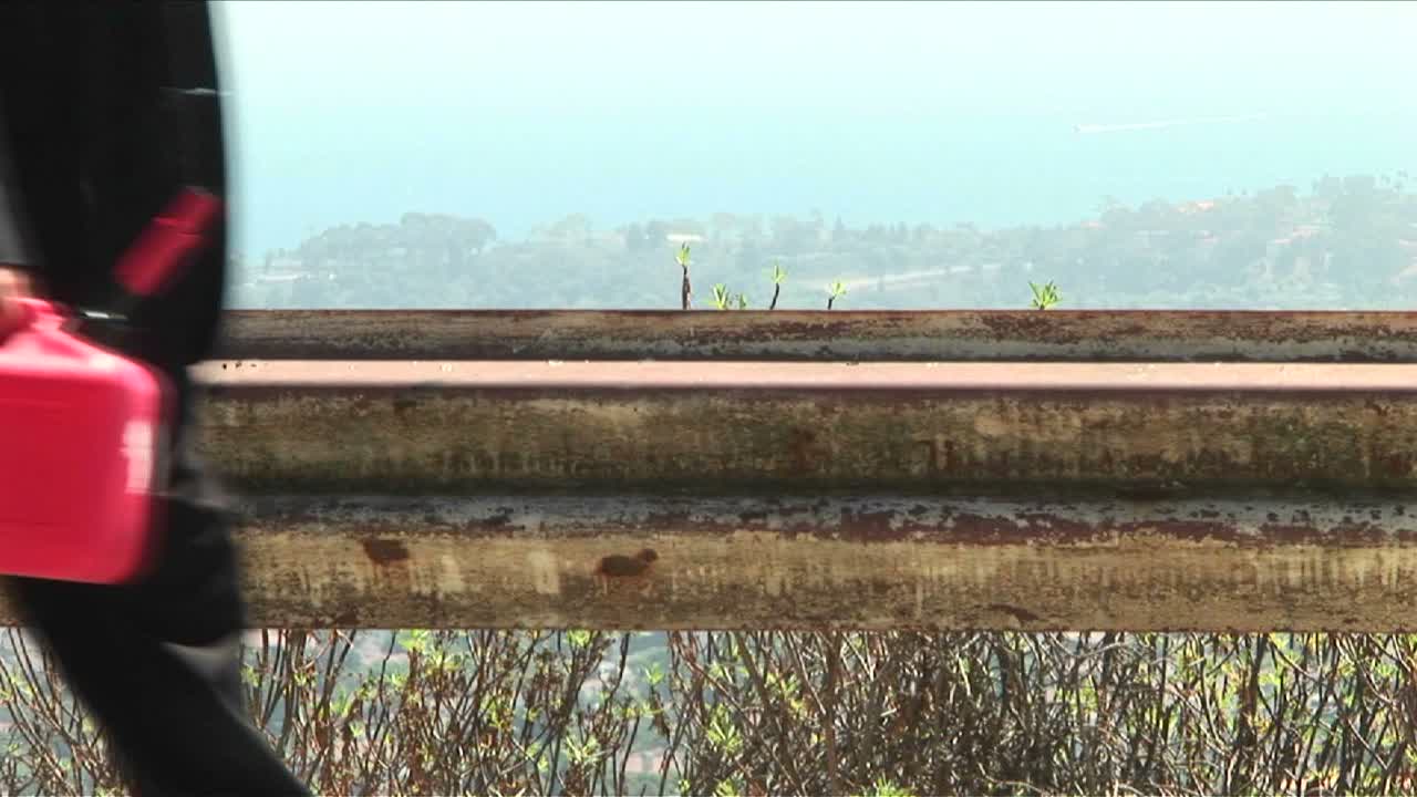 한 남자가 밝은 빨간색 가스통을 들고 길을 걷고 있다