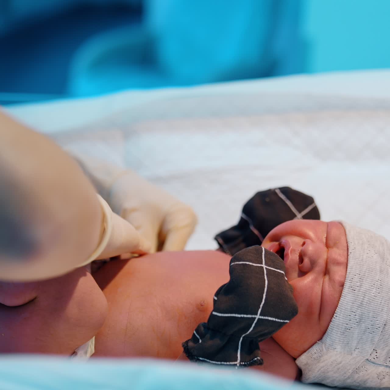 Neonato appena nato che piange disperatamente sul tavolo. Il neonato indossa un cappellino, guanti, calzini e un pannolino