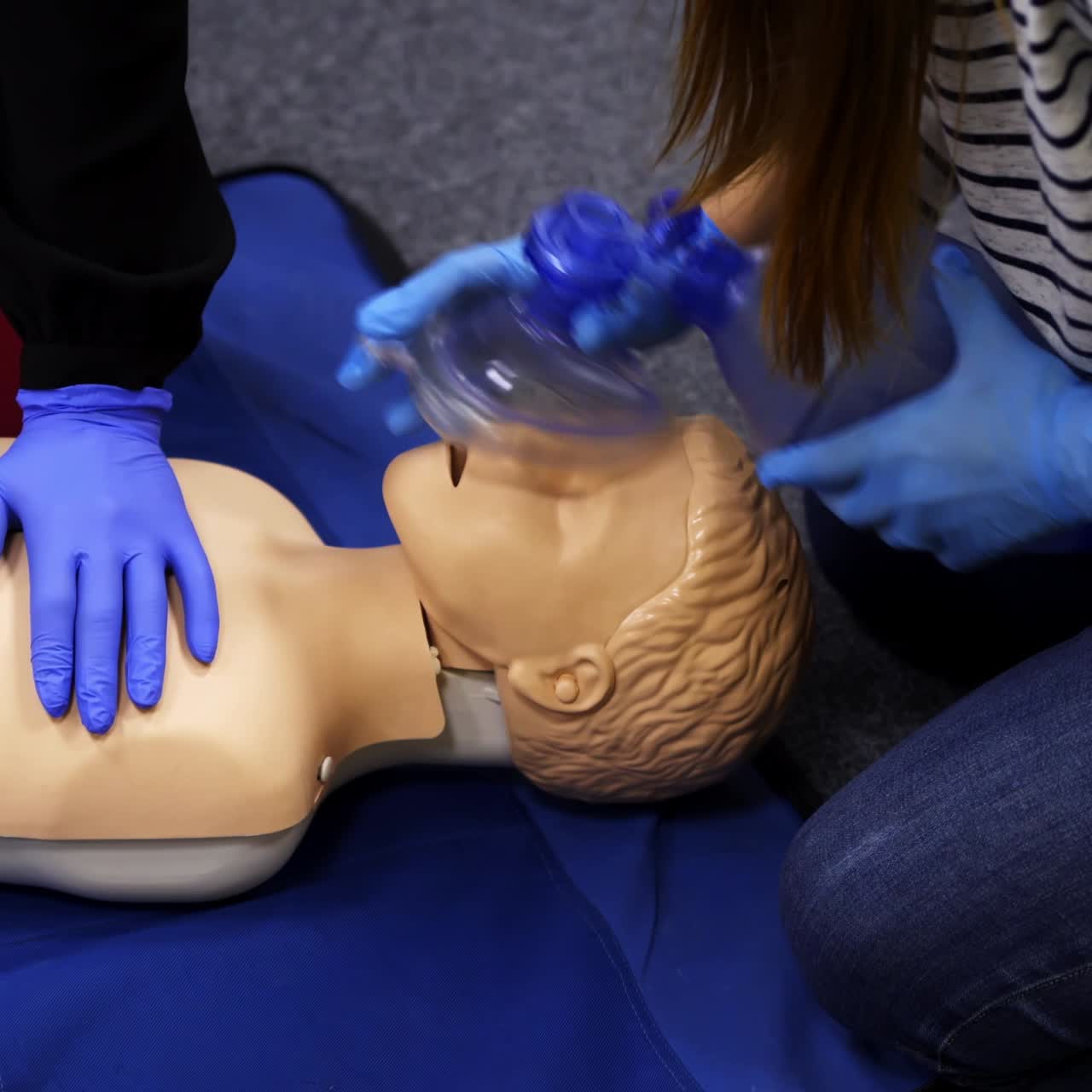 Training reanimation procedure on a mannequin. People use breathing apparatus on a dummy's face during practice course. Training for giving first aid to a patient.