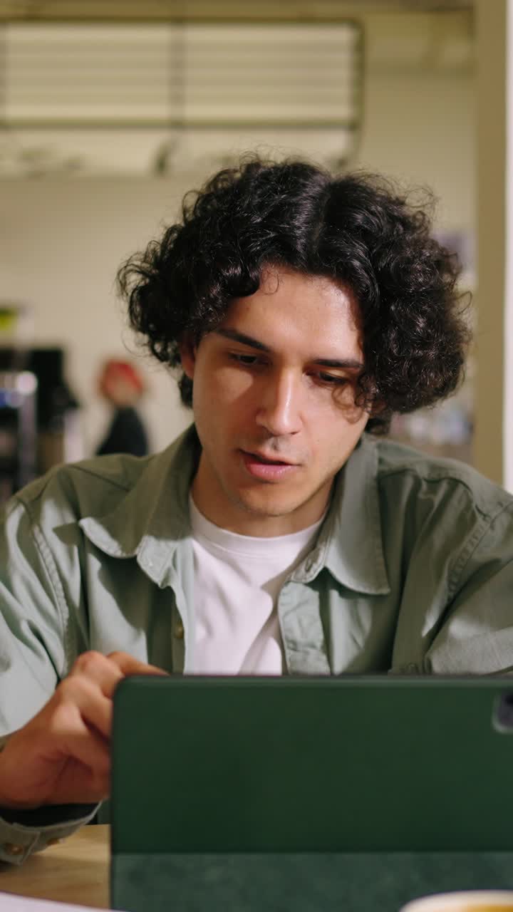 Young Man Working and Smiling on Tablet in a Cafe