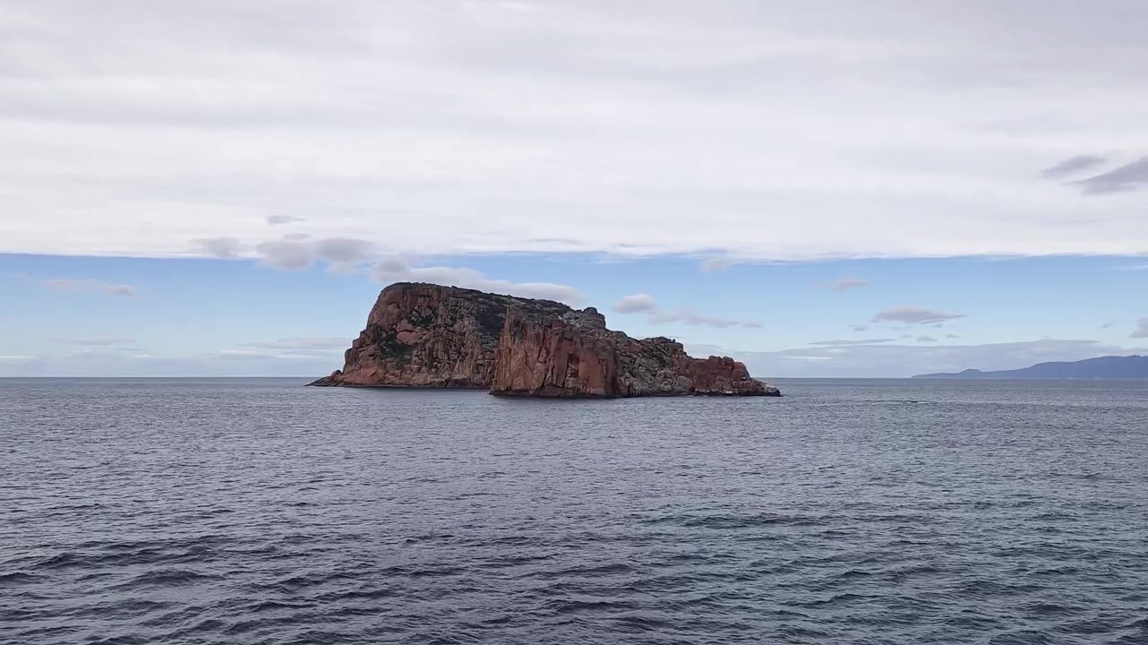 Isola rocciosa remota nell'oceano calmo sotto un cielo nuvoloso