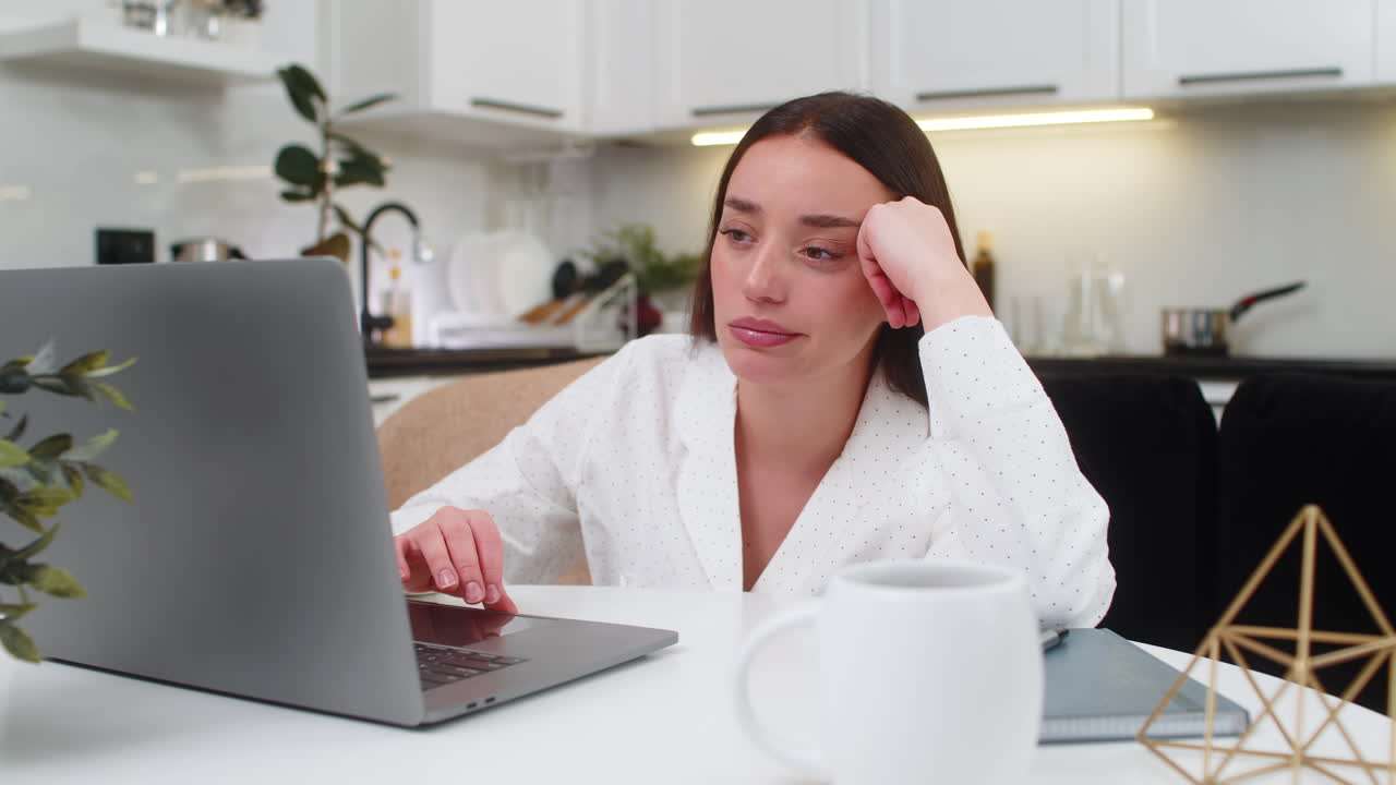 Young woman bored at laptop leans on hand tired unhappy burnout low energy focus lost work slump