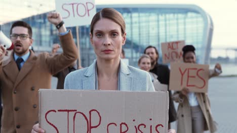 die kamera zoomt heraus auf eine kaukasische frau, die bei einem protest mit multiethnischen geschäftskollegen auf der straße ein „stop crisis“-schild hält.