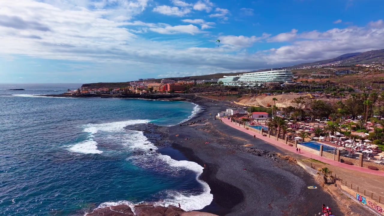 Vista aérea de una playa de arena negra, olas del océano y el paseo marítimo del resort en un día soleado