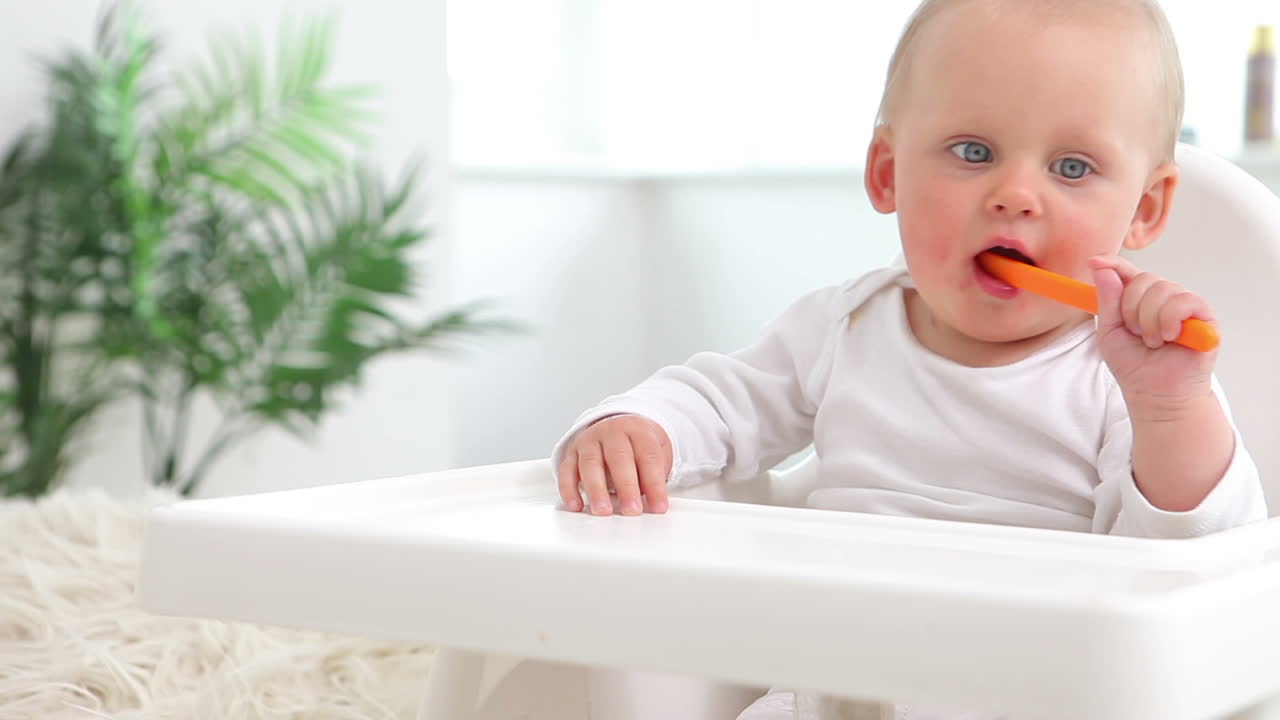 Baby sitting and bites orange spoon