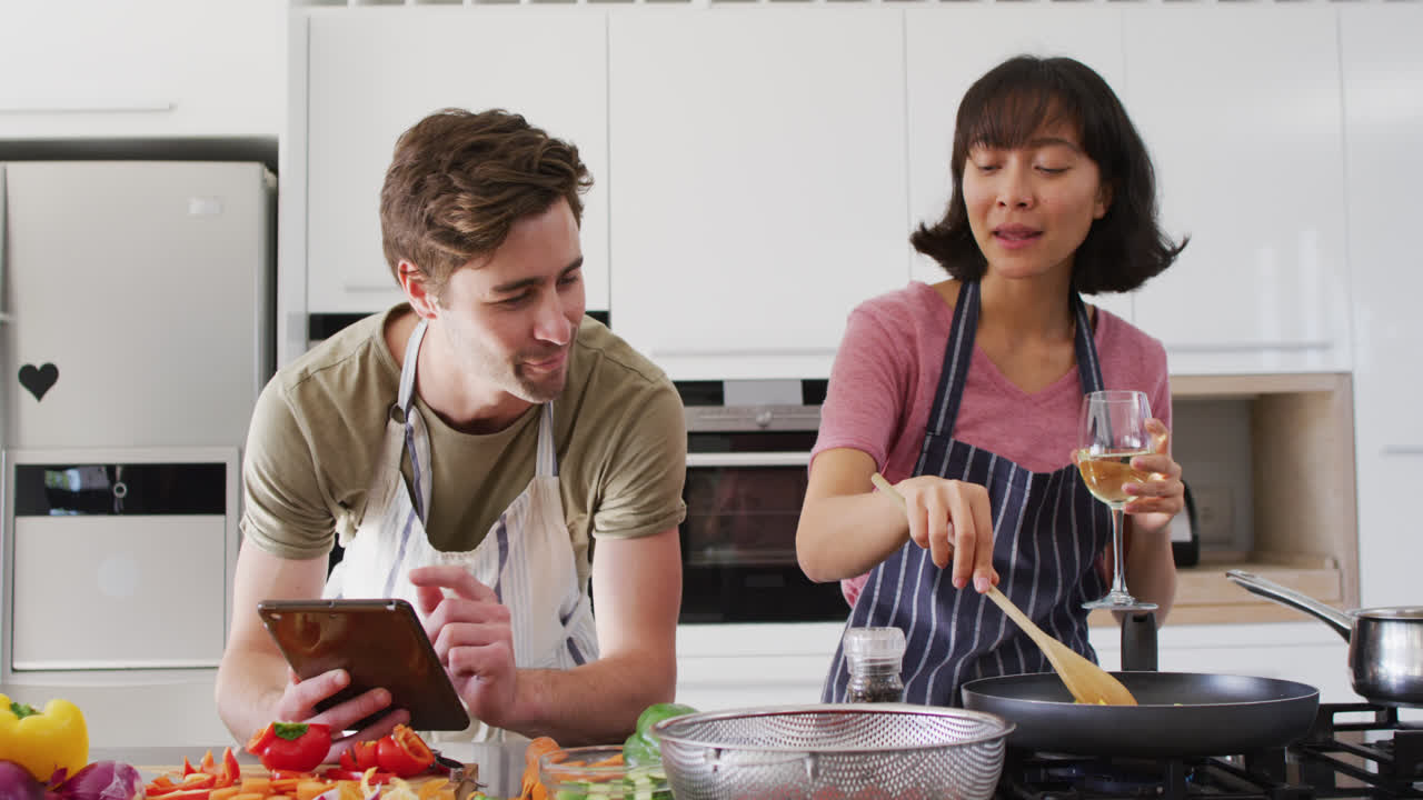 video de una pareja feliz y diversa preparando una comida juntos con una tableta y vino