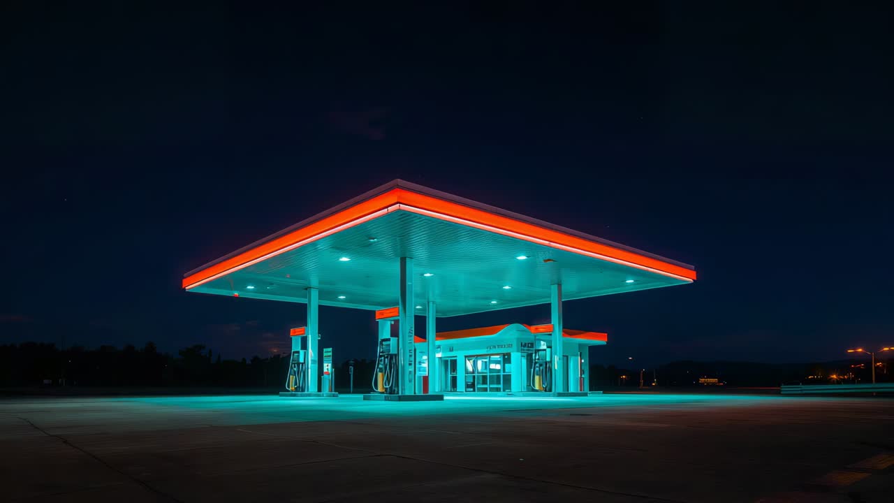 Framing camera zooming toward fuel canopy with pumps at night, showing teal lights on forecourt