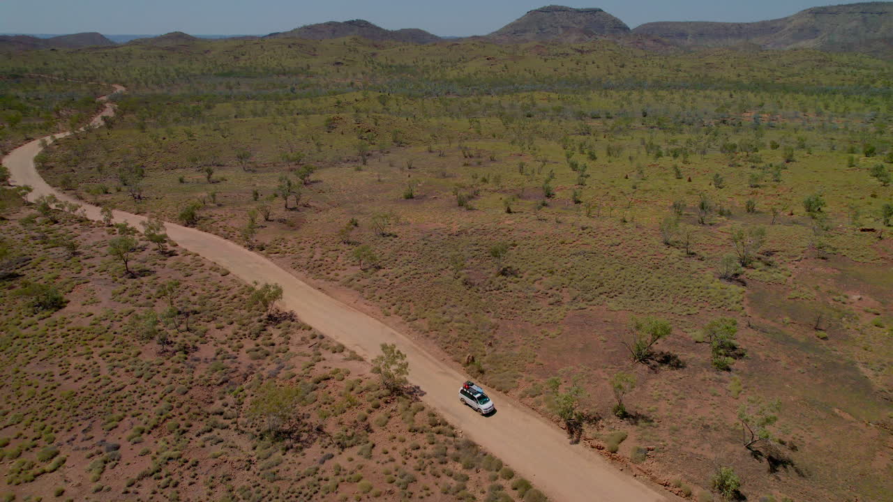 Ripresa aerea con drone che segue un veicolo 4x4 mentre percorre una strada sterrata remota lasciando le Bungle Bungles nel Parco Nazionale Purnululu, Australia Occidentale. Paesaggio aspro dell'outback, viaggi d'avventura