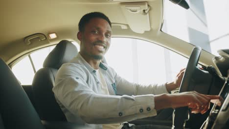 a man tests a new car. side view of focused african man sitting on driver's seat and using dashboard for navigation. man pressing touchscreen on car multimedia panel, switching shifting radio station