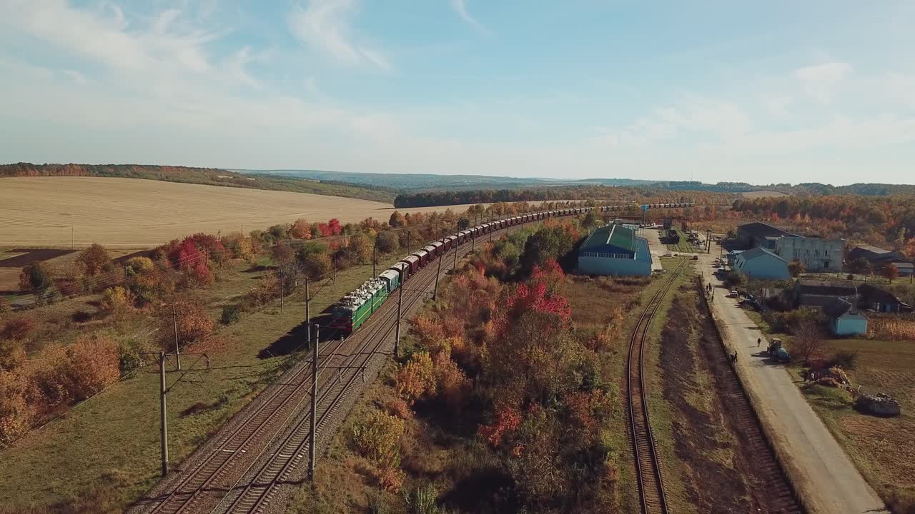 freight train is moving by rail to the nearest town on the background of the countryside with fields and road. Aerial view