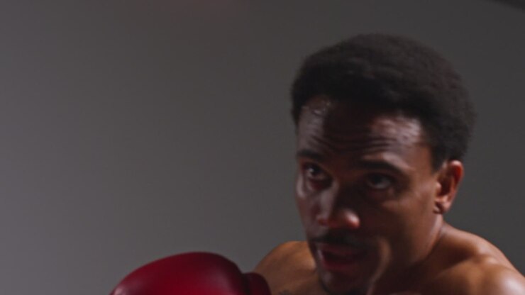 Close Up Studio Shot Of Tattooed Male Boxer Wearing Boxing Gloves In Boxing Match Throwing Punches