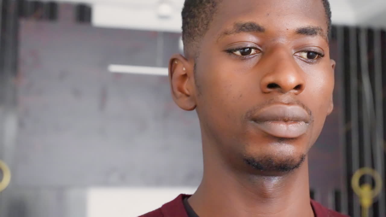 Black man closeup in studio, painted wall backdrop and soft light, contemplative expression with subtle gaze, cinematic moody portrait of young black painter and creative thinking