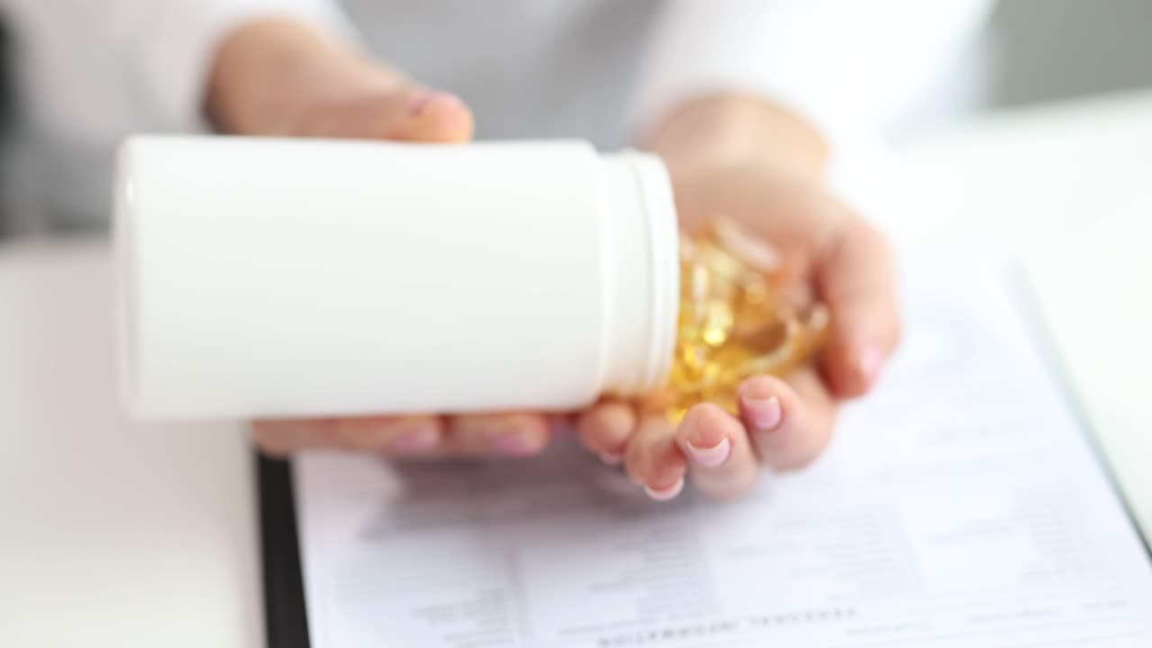 Hands Pouring Yellow Capsules from a White Bottle