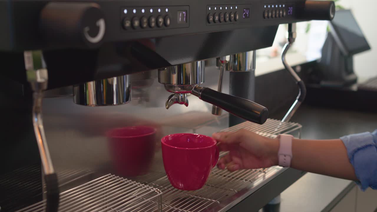 Dopo lo scatto, barista che pulisce il portafiltro e versa l’espresso in una tazza rossa al bancone del bar