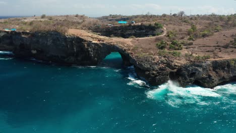 Arco-Natural-Y-Agujero-En-La-Isla-De-Nusa-Penida,-Bali,-Indonesia,-Retroceso-Aéreo