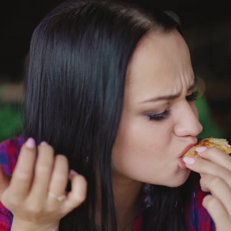 beautiful brunette in a plaid shirt is eating pizza with enjoy in the cafe on the background of the interior