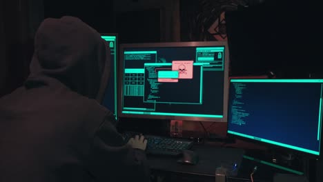 hacker in a hood sits in front of computer screens and hacks databases
