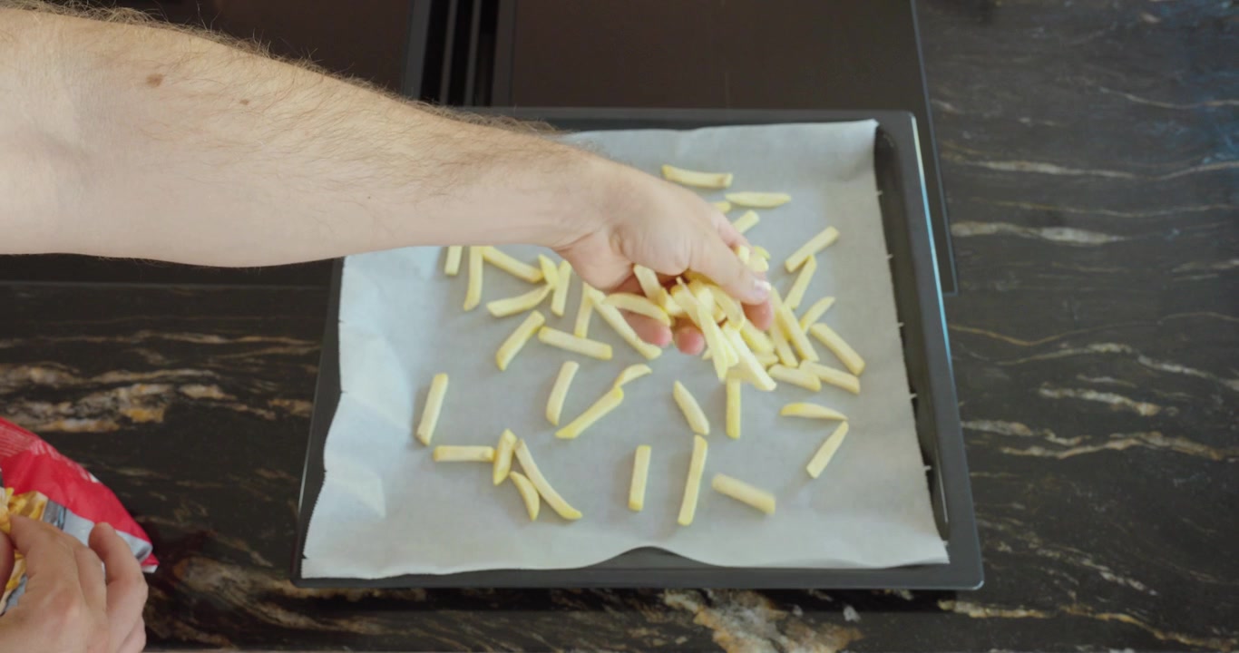 Person spreading frozen French fries on a baking tray before cooking in the oven. Ideal for easy meals, fast food and home cooking.