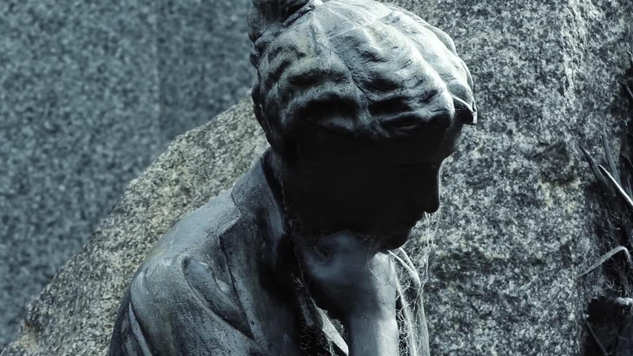 Primo piano di una statua di bronzo pensierosa con la testa china.