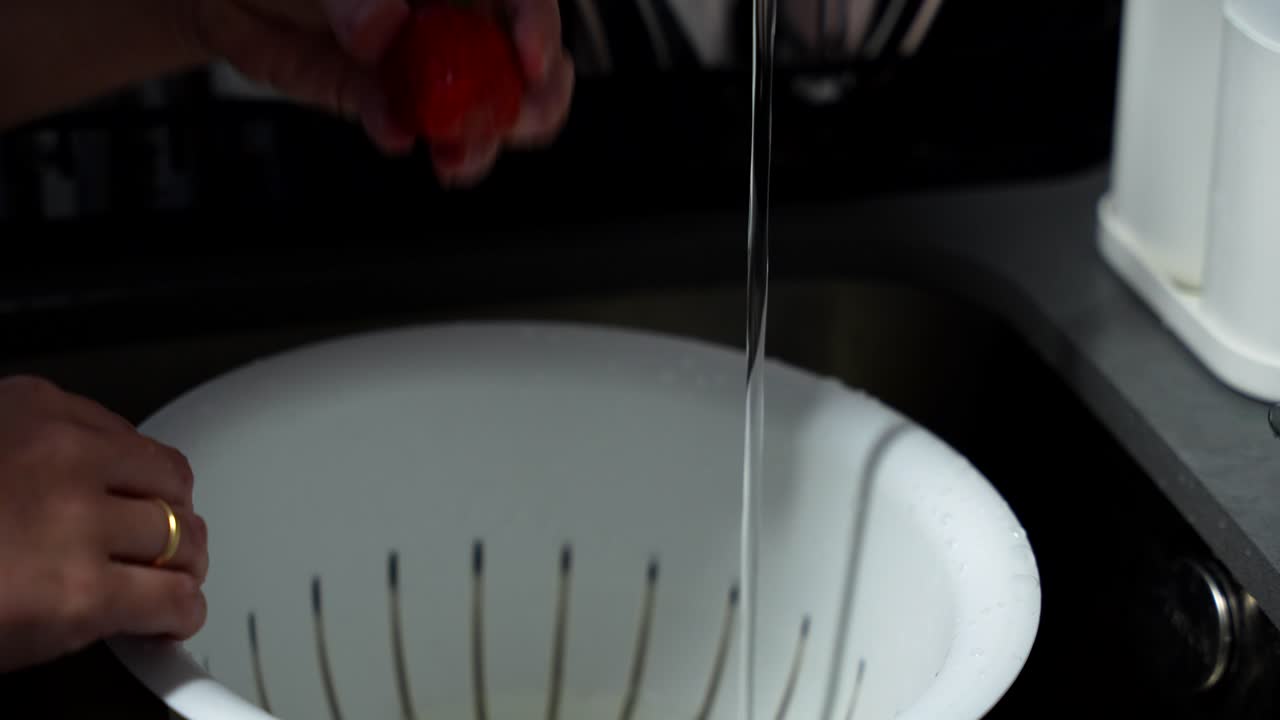 Female hands opening the tap to clean red strawberries in the sink