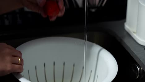 female hands opening the tap to clean red strawberries in the sink