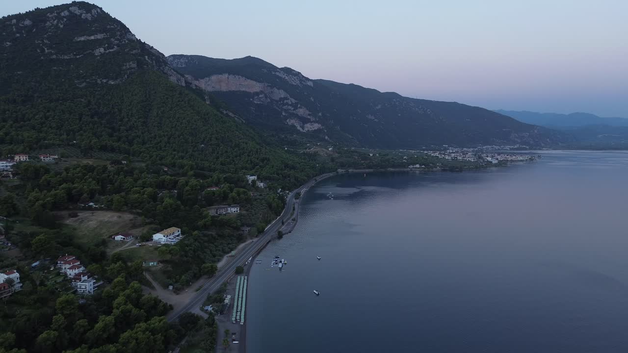 Drone flight along the coast in Greece, showcasing villages and mountains in the early morning before sunrise