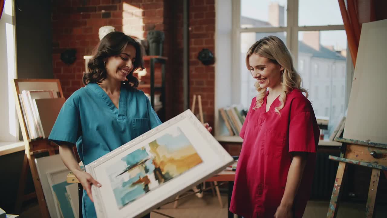 Presentazione di una donna in camice blu che ruota un dipinto astratto su un cavalletto in studio, indicandolo per la revisione