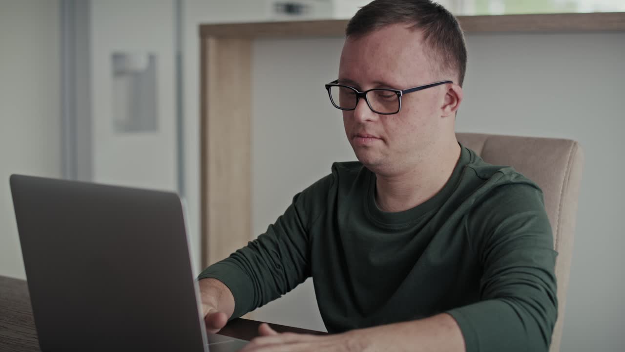 Focus adult caucasian man with down syndrome typing on laptop at home.
