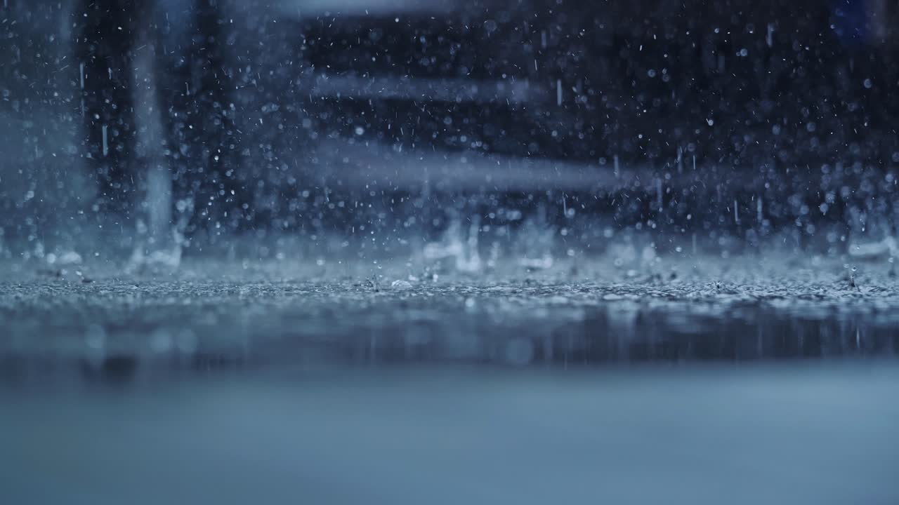 Slow motion captures heavy rain hitting asphalt from a low static camera angle