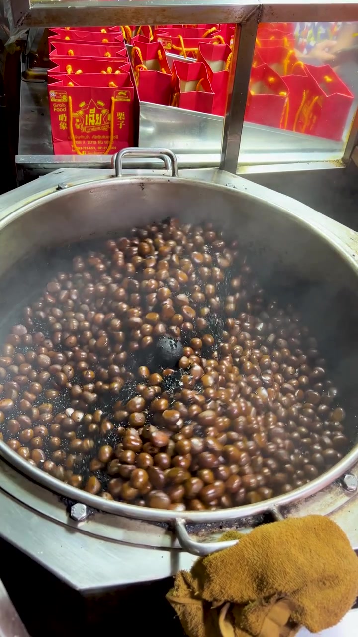 Chestnuts roasting and stirring in large metal pan, vibrant night market lighting, shallow depth