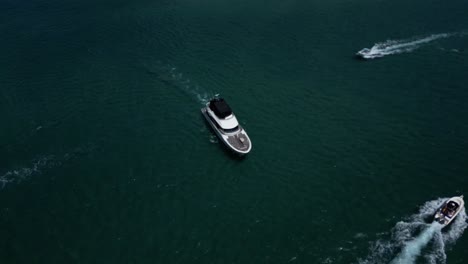 a luxury yacht moving slowly navigating between smaller boats on a river from an aerial drone perspective looking down on the water below
