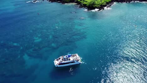 a drone, birds eye, aerial view of a party boat on the the beautiful teal waters along the coast of wailea beaches on the island of maui, hawaii