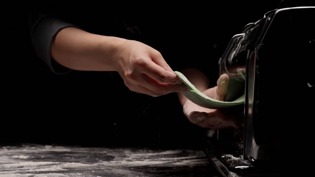 Primo piano di mani che preparano pasta fresca verde con una macchina