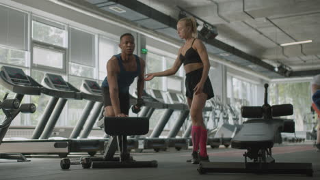 una mujer caucásica y un atlético afroamericano en el gimnasio.