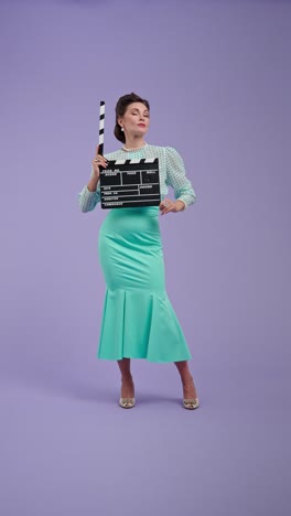 woman in vintage outfit holding movie clapperboard on purple background