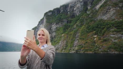 a woman takes pictures of herself against the backdrop of the norwegian fjord travelling on a cruise