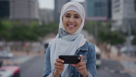 Retrato-De-Una-Joven-Estudiante-Musulmana-Usando-Un-Teléfono-Inteligente-En-La-Ciudad-Disfrutando-De-Mensajes-De-Texto,-Navegando-Por-Mensajes-Viendo-Entretenimiento-En-Un-Teléfono-Móvil-Usando-Un-Velo-Hijab