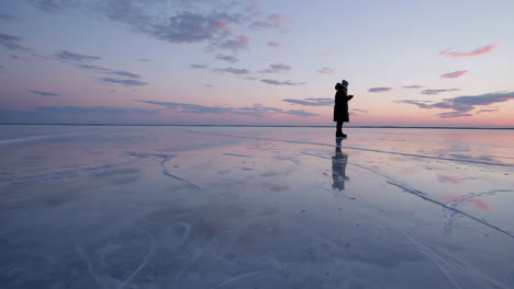 a lone figure stands on a vast, reflective frozen landscape under a colorful twilight sky