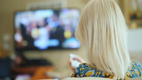 a woman is watching tv in the living room rear view holds a remote control 4k video