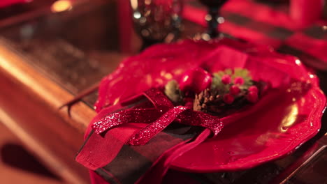 festive red plate with wavy edges and christmas decoration on top. artificial greenery and berries tied up with sparkling red ribbon. blurred backdrop.