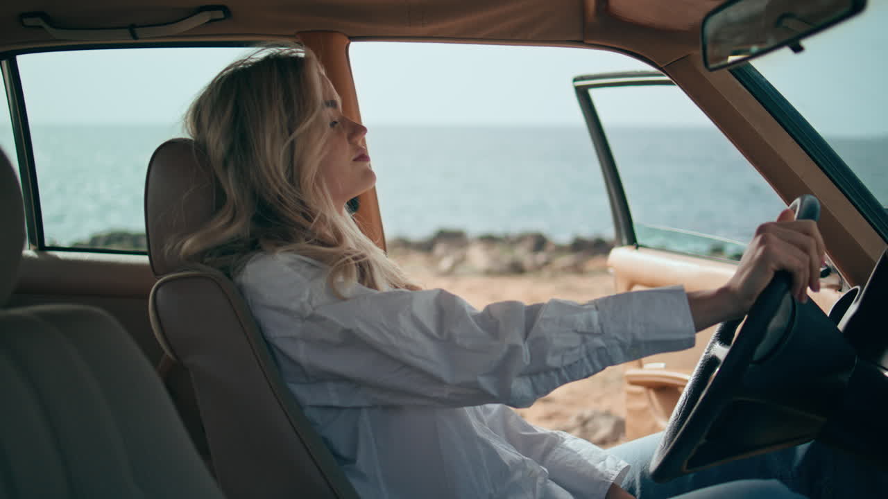 바다 연안에 차를 타고 앉아 있는 걱정스러운 여자. 금발의 바가 뛰고 있다.