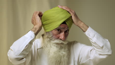 Fotografía-De-Estudio-De-Un-Hombre-Sikh-Mayor-Con-Barba-Atando-Una-Tela-Para-Un-Turbante-Contra-Un-Fondo-Liso,-Filmada-En-Tiempo-Real-2